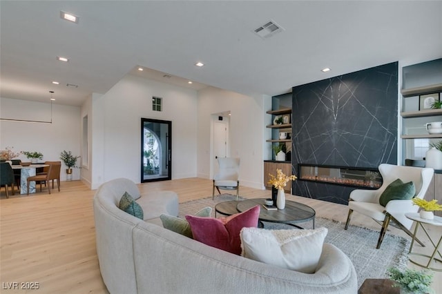 living area featuring visible vents, a high end fireplace, an accent wall, wood finished floors, and recessed lighting