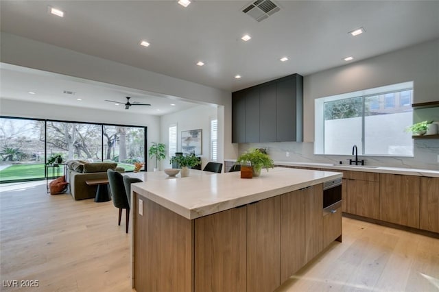 kitchen with light wood finished floors, visible vents, a kitchen island, a sink, and modern cabinets