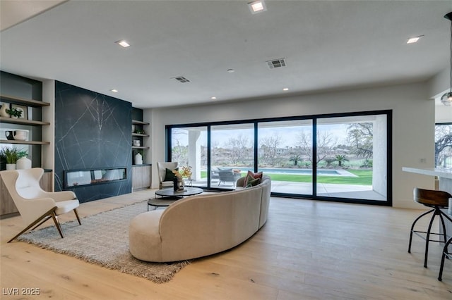 living room with built in shelves, a premium fireplace, wood finished floors, and visible vents