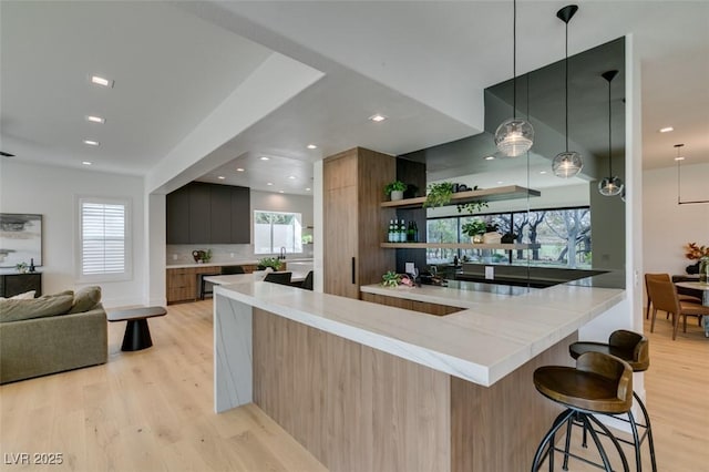 kitchen with hanging light fixtures, light wood finished floors, modern cabinets, and a kitchen breakfast bar