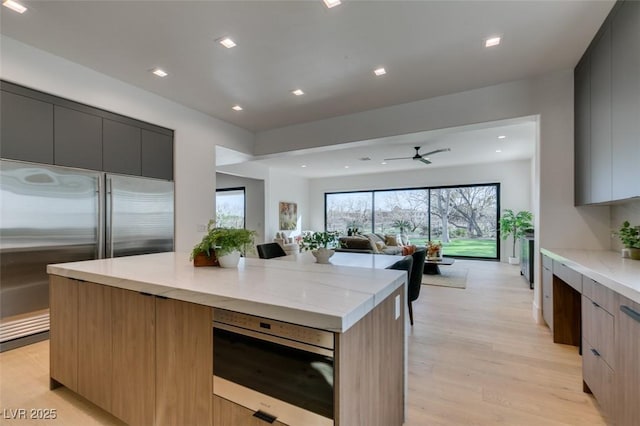 kitchen with light wood-type flooring, modern cabinets, a kitchen island, and stainless steel built in refrigerator