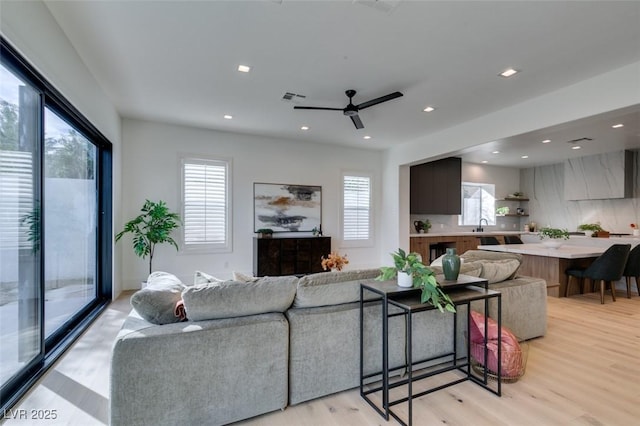 living room featuring a ceiling fan, light wood-type flooring, visible vents, and recessed lighting