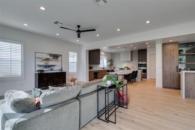 living room featuring ceiling fan, light wood finished floors, visible vents, and recessed lighting