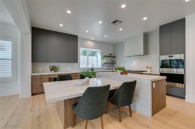 kitchen featuring a spacious island, visible vents, wall chimney range hood, light wood-type flooring, and modern cabinets