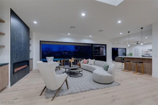 living room featuring built in features, a fireplace, recessed lighting, visible vents, and light wood-style flooring