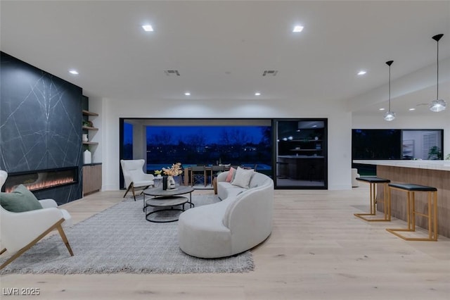 living area with a premium fireplace, light wood-type flooring, visible vents, and recessed lighting