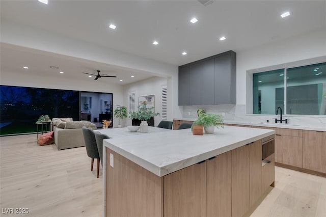 kitchen with light brown cabinetry, a kitchen island, a sink, modern cabinets, and light wood-type flooring