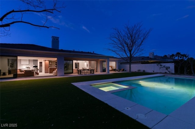 pool at night featuring a pool with connected hot tub and a patio