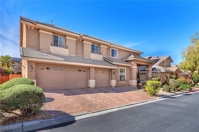 view of front facade with a garage, a tiled roof, decorative driveway, and stucco siding