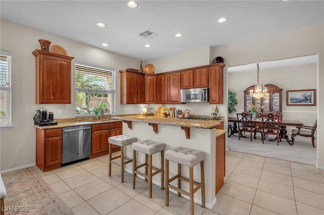 kitchen with stainless steel appliances, a breakfast bar, a sink, visible vents, and light stone countertops