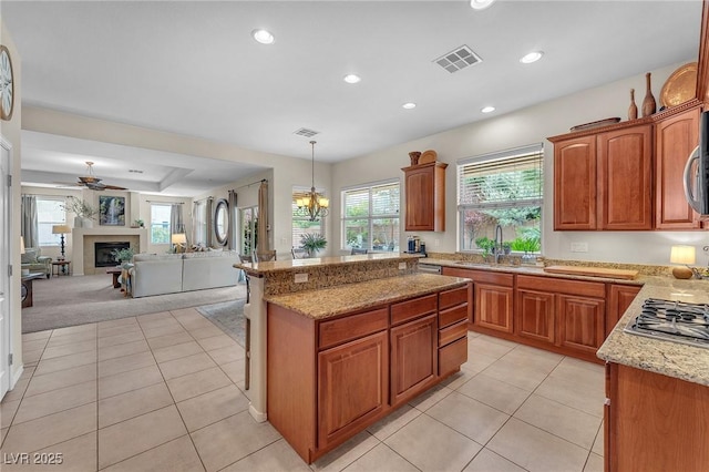 kitchen with light tile patterned floors, visible vents, a glass covered fireplace, a sink, and light stone countertops