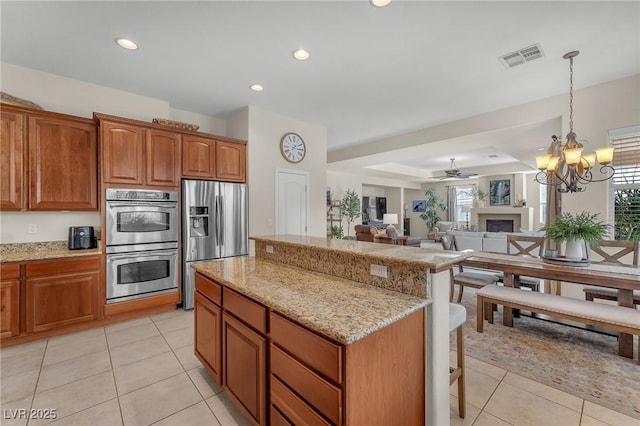 kitchen with light tile patterned floors, light stone counters, stainless steel appliances, and a center island