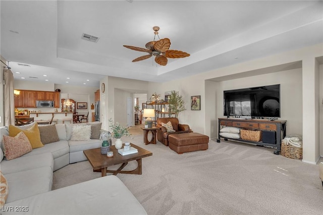 living area with ceiling fan, recessed lighting, light colored carpet, visible vents, and a raised ceiling