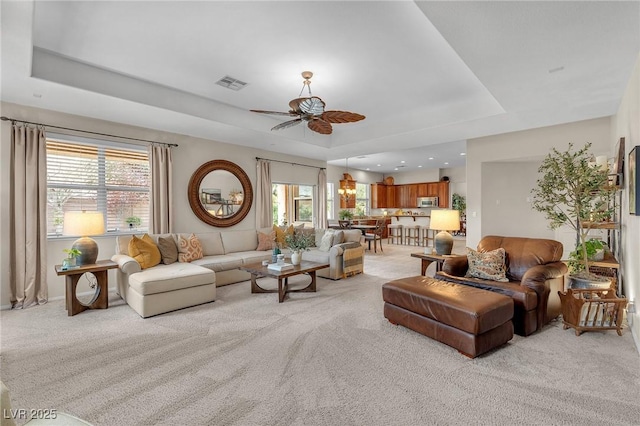 living room featuring light carpet, ceiling fan, visible vents, and a raised ceiling