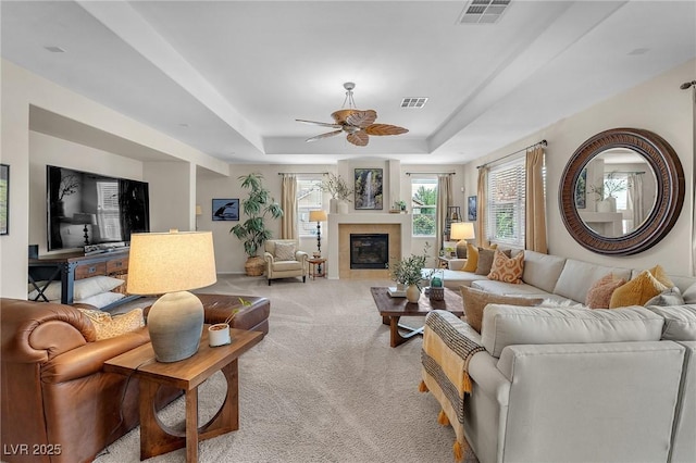 living room featuring a tile fireplace, visible vents, a tray ceiling, and light colored carpet