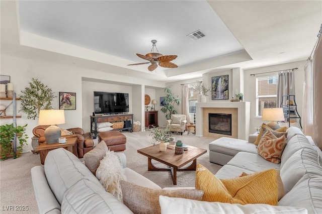 living area featuring visible vents, a raised ceiling, ceiling fan, carpet flooring, and a fireplace