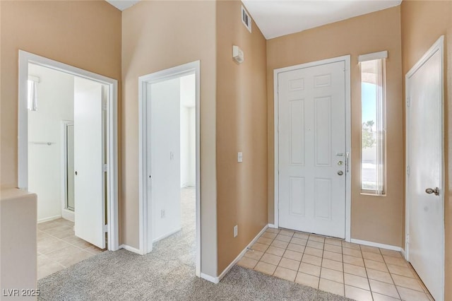 foyer with a wealth of natural light, light tile patterned flooring, visible vents, and light colored carpet