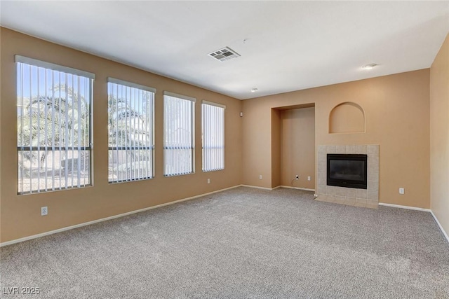 unfurnished living room with carpet floors, baseboards, visible vents, and a tiled fireplace