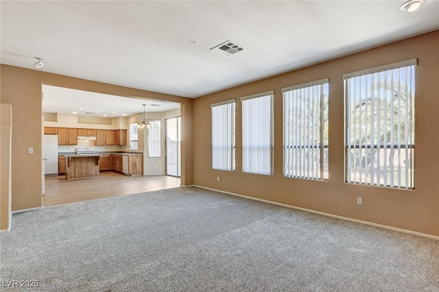 unfurnished living room with visible vents, light carpet, baseboards, and an inviting chandelier