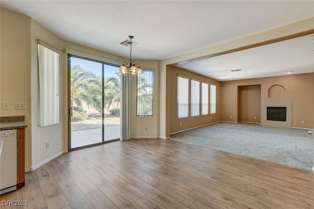 unfurnished living room with a wealth of natural light, a glass covered fireplace, light wood-type flooring, and visible vents