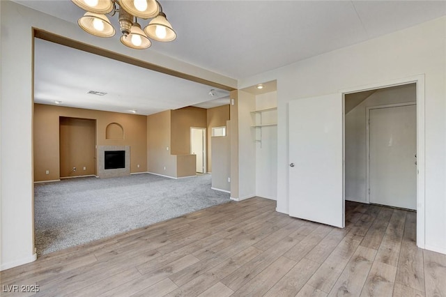 unfurnished living room featuring a fireplace, carpet flooring, wood finished floors, visible vents, and baseboards