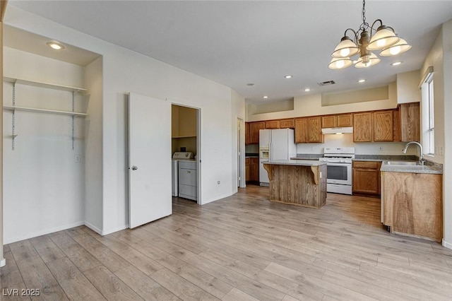 kitchen with under cabinet range hood, separate washer and dryer, white appliances, a sink, and visible vents