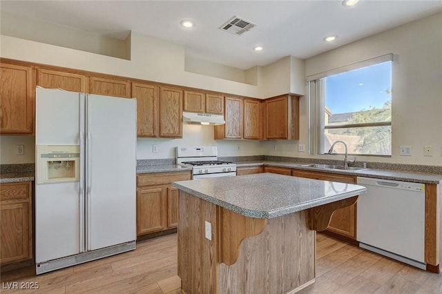 kitchen featuring under cabinet range hood, white appliances, a sink, visible vents, and light wood-type flooring