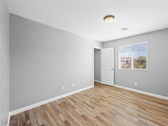 empty room with light wood-type flooring, visible vents, and baseboards