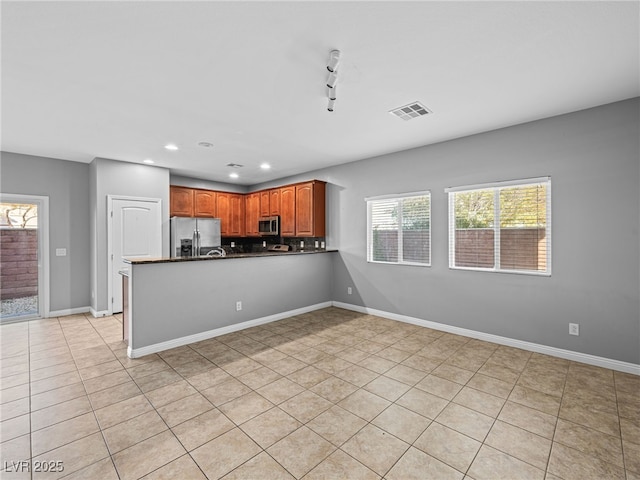 kitchen with brown cabinets, stainless steel appliances, dark countertops, visible vents, and a peninsula