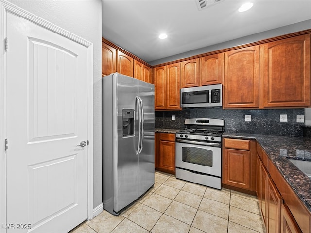 kitchen with light tile patterned floors, appliances with stainless steel finishes, dark stone countertops, and tasteful backsplash