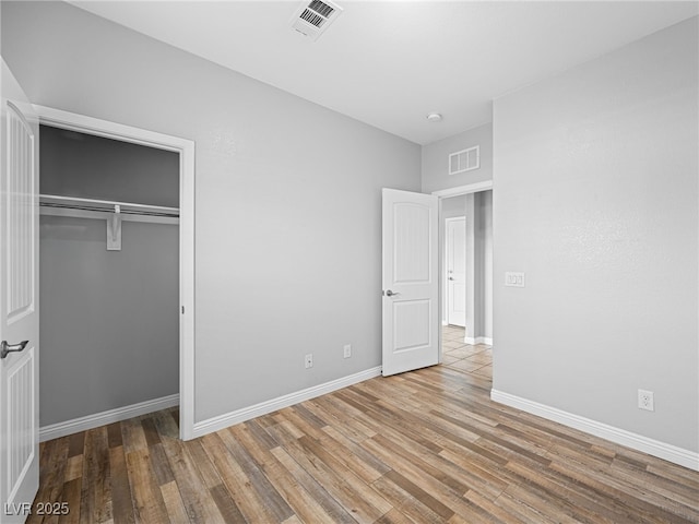 unfurnished bedroom with a closet, visible vents, baseboards, and wood finished floors