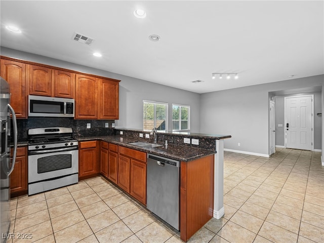 kitchen featuring a peninsula, a sink, visible vents, appliances with stainless steel finishes, and dark stone counters