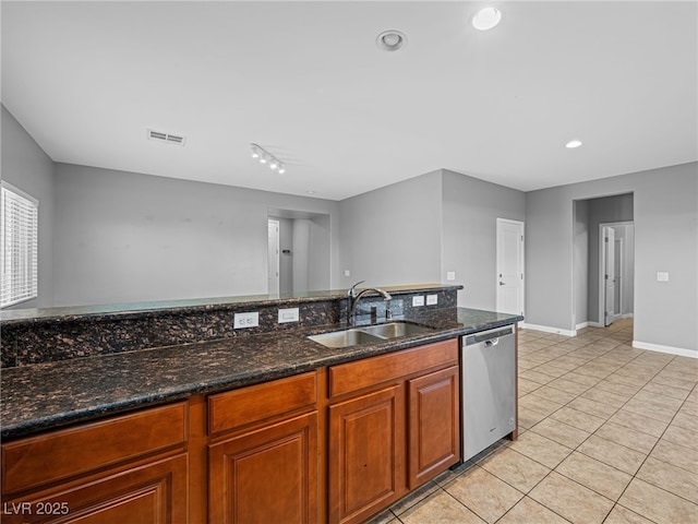 kitchen with brown cabinets, light tile patterned floors, stainless steel dishwasher, a sink, and dark stone countertops