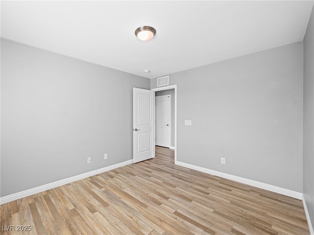 spare room with light wood-type flooring, visible vents, and baseboards