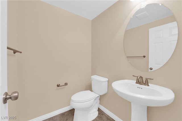 half bathroom with a sink, tile patterned flooring, toilet, and baseboards