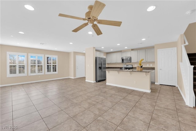 kitchen with ceiling fan, a kitchen island with sink, stainless steel appliances, open floor plan, and a kitchen bar