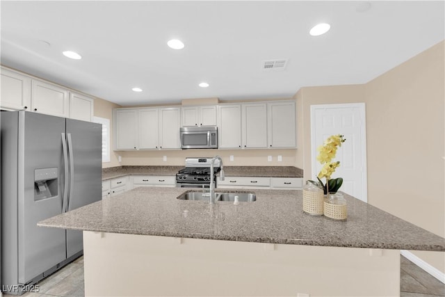 kitchen with a center island with sink, stainless steel appliances, visible vents, a sink, and dark stone countertops