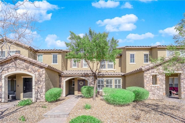 mediterranean / spanish-style home with stone siding, a tiled roof, and stucco siding