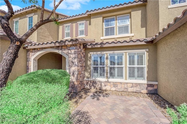 exterior space featuring stone siding, a tiled roof, and stucco siding