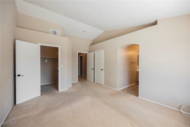 unfurnished bedroom with light carpet, visible vents, arched walkways, connected bathroom, and lofted ceiling