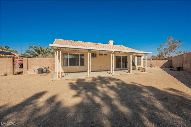 rear view of house featuring a patio, a fenced backyard, a tile roof, a gate, and stucco siding