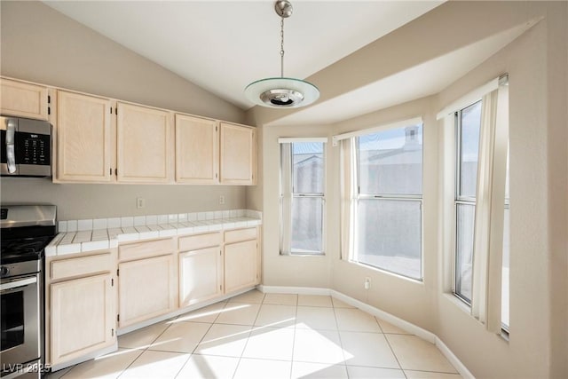 kitchen featuring baseboards, tile countertops, lofted ceiling, appliances with stainless steel finishes, and hanging light fixtures