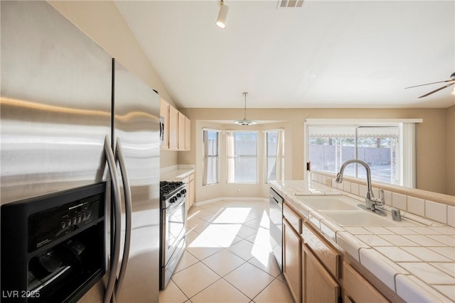 kitchen featuring light tile patterned floors, stainless steel appliances, a sink, tile counters, and pendant lighting