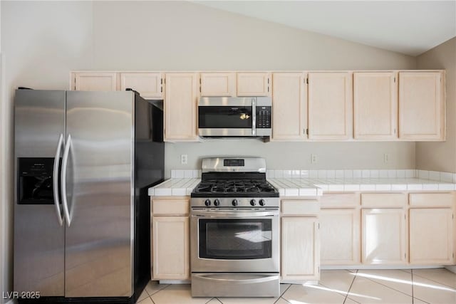 kitchen with appliances with stainless steel finishes, tile counters, vaulted ceiling, and light tile patterned floors