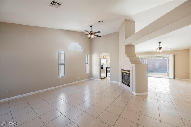 unfurnished living room featuring light tile patterned floors, visible vents, a ceiling fan, a tile fireplace, and baseboards