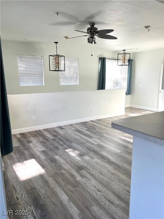 interior space featuring ceiling fan, a textured ceiling, baseboards, and wood finished floors