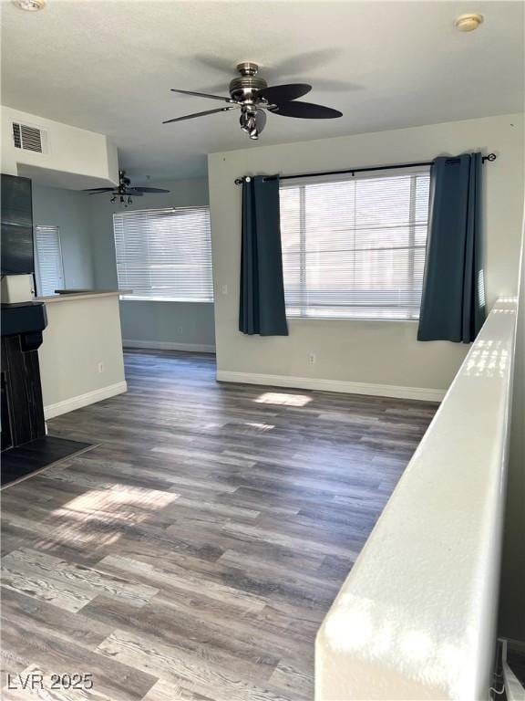 unfurnished living room featuring a ceiling fan, baseboards, visible vents, and wood finished floors