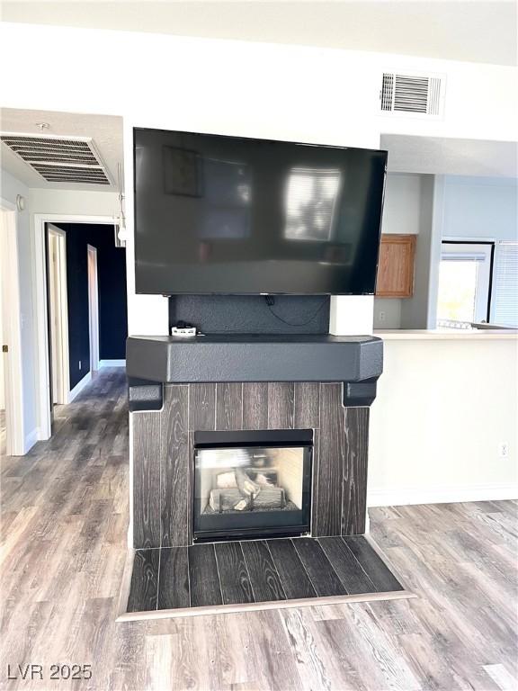 interior details with a glass covered fireplace, visible vents, baseboards, and wood finished floors