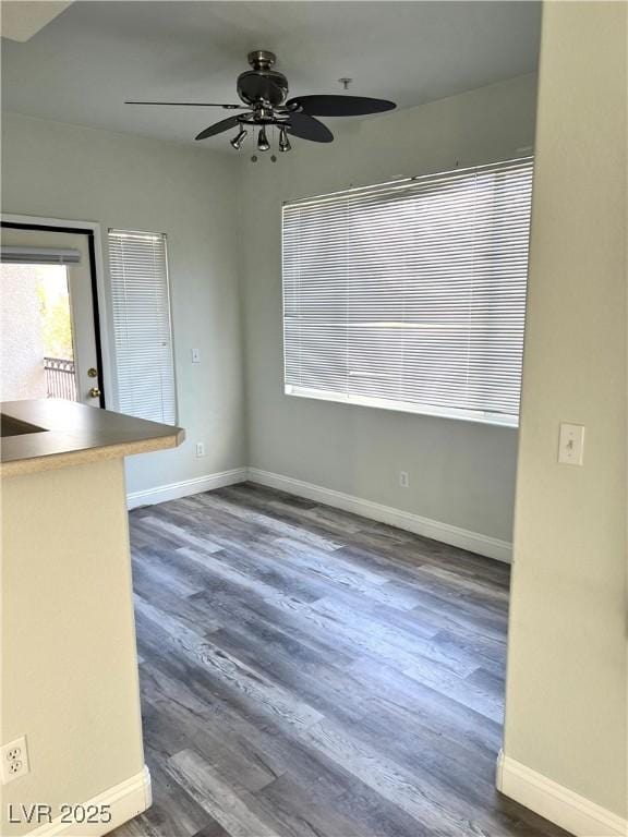 unfurnished dining area with dark wood-style flooring, ceiling fan, and baseboards