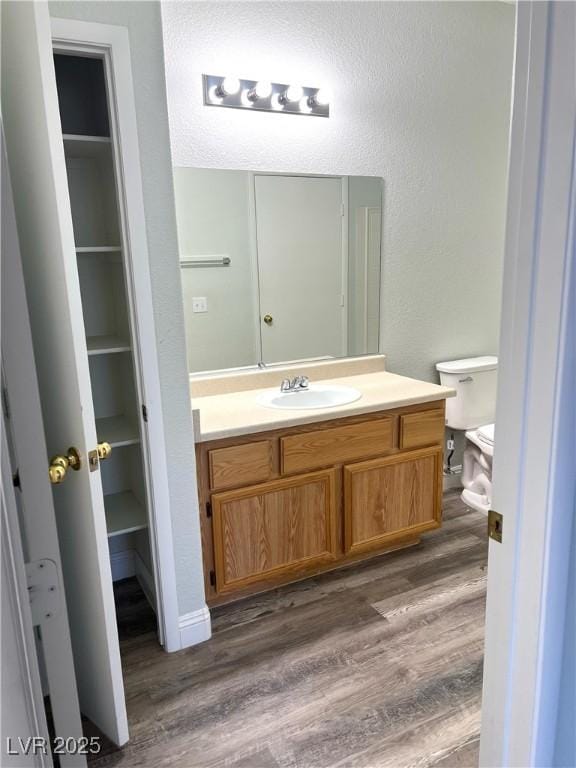 bathroom featuring toilet, a textured wall, wood finished floors, and vanity